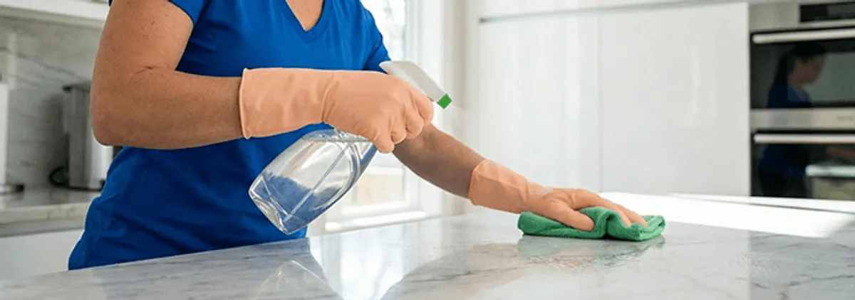 Maid service worker spraying and wiping a kitchen countertop with a microfiber cloth for sanitizing, Knoxville, TN.
